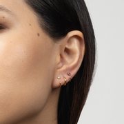 Close-up of an ear wearing gold Stay Close Aquamarine Hoops with a plain background