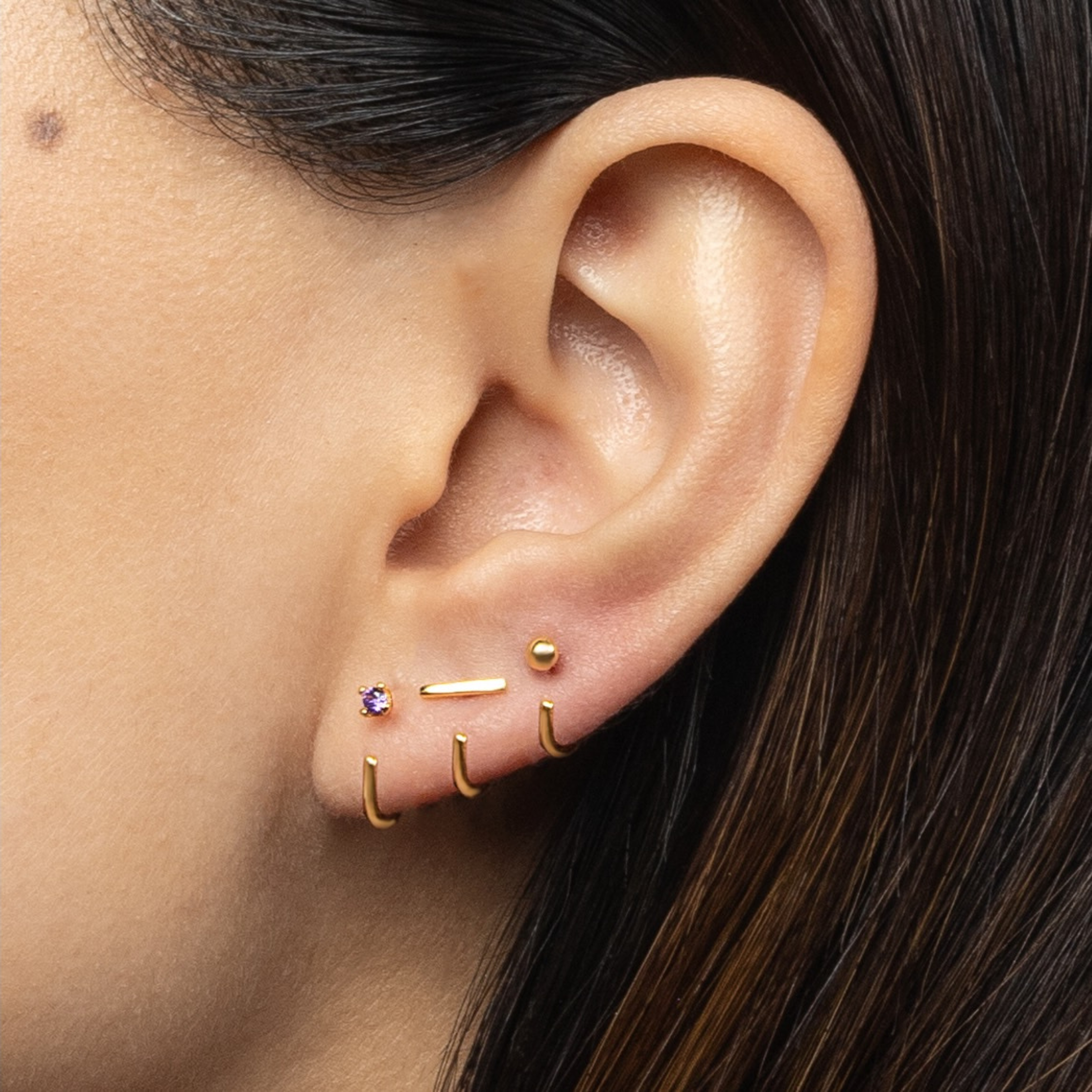 Close-up of an ear wearing gold Stay Close Amethyst Hoops