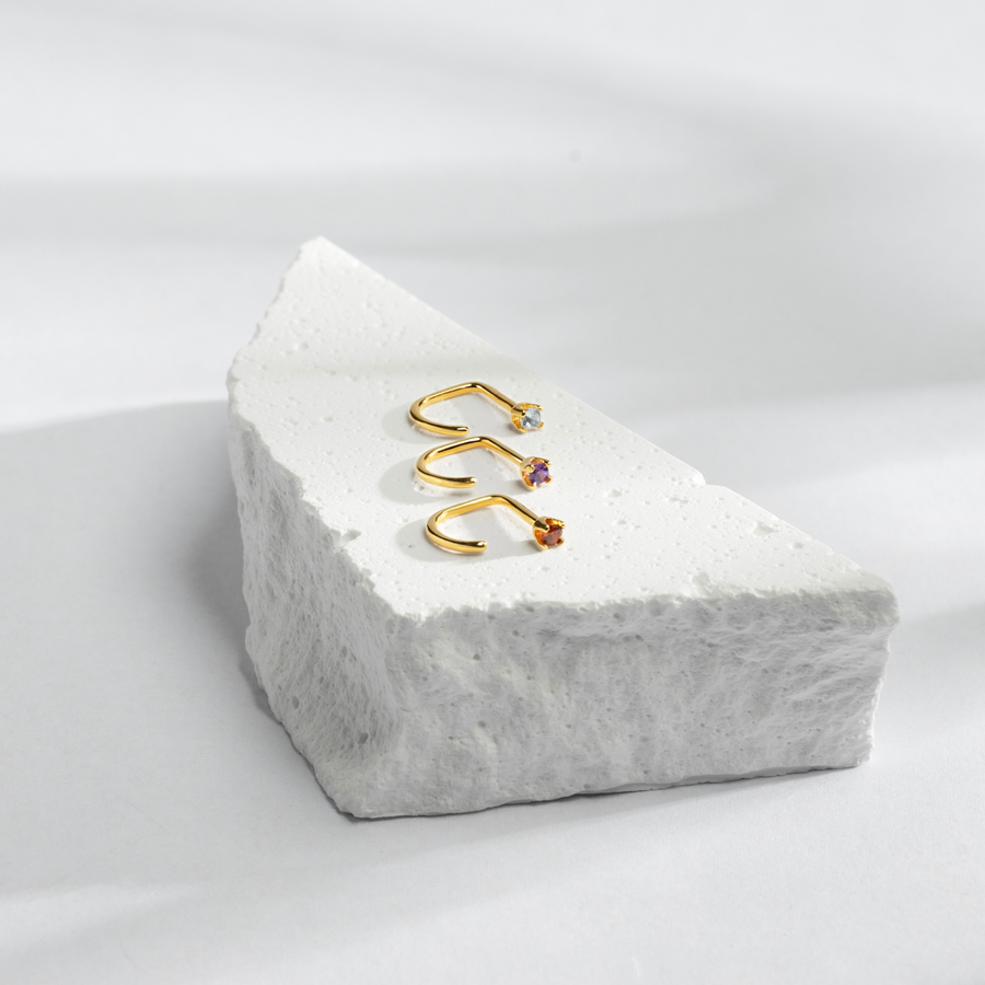 Gold Stay Close Hoops with gemstones on a white stone block against a light gray background