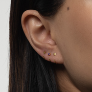 Close-up of an ear with gold Stay Close Amethyst Hoop on a neutral background