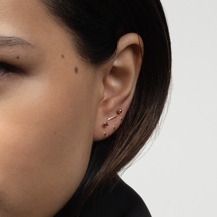 Close-up of a person wearing an Stay Close Amethyst Hoop on a plain background