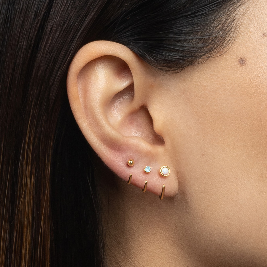 Close-up of an ear wearing multiple gold Stay Close Hoops with gemstones.