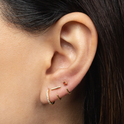 Close-up of an ear wearing a Stay Close Garnet Hoop with a red gemstone.